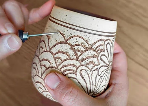 Engraving ceramic cup with handheld engraving tool.