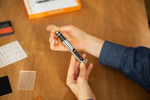 Person holding electric engraving pen for DIY craft projects.